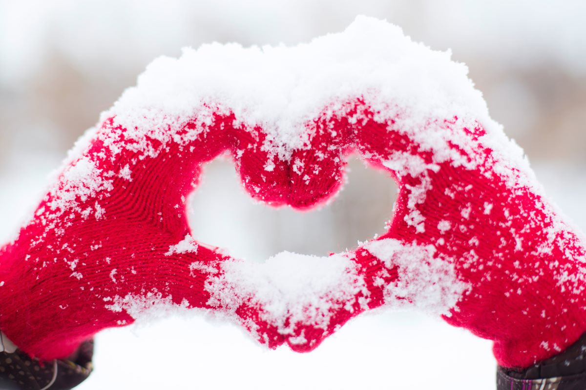 Two hands wearing red gloves forming a shape of a heart with snow covering the gloves 